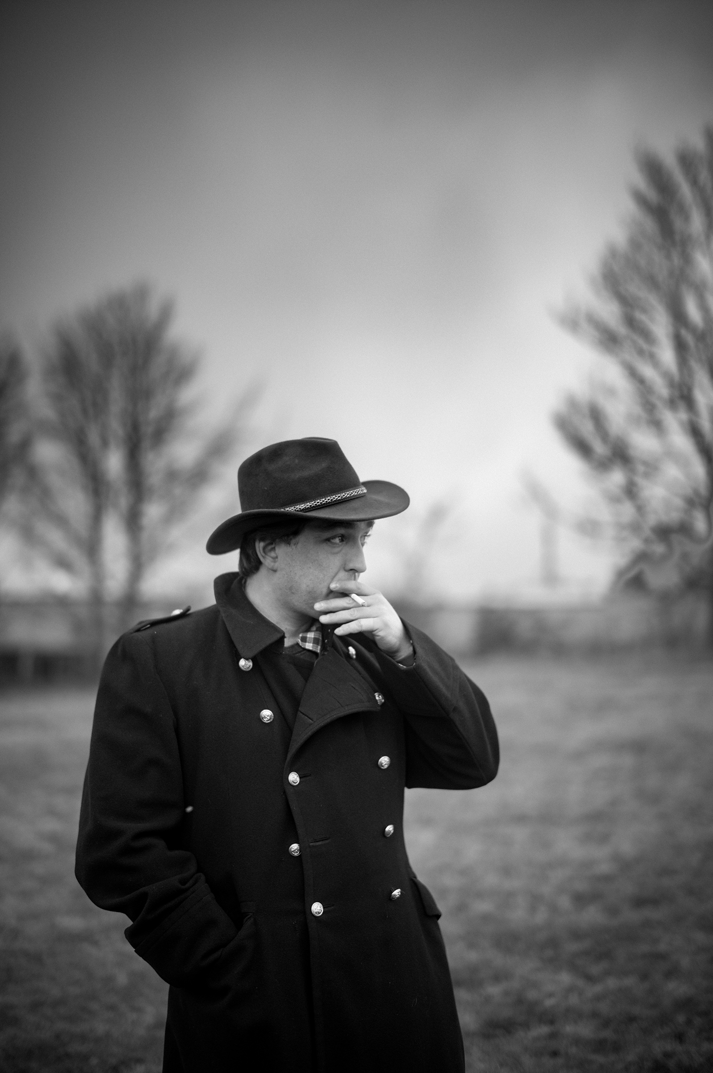Mann mit Hut und dunklem Mantel auf einem Feld – Schwarz-Weiß-Fotografie von Bernhard Brause